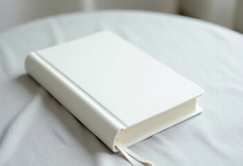 Fototapeta premium A pristine white blank notebook rests on a light gray fabric surface.
