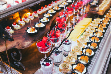 An elegant buffet table featuring a variety of appetizers, desserts, and fruits served in small portions. Perfect for event catering, food presentation, or fine dining concepts.