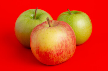 Three red apples and two green ones on a red background.