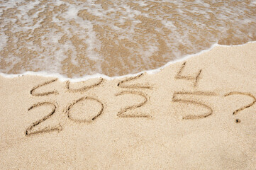 Inscription 2024 and 2025 numbers written on sand with question mark. Concept image