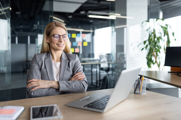 A professional businesswoman confidently sitting at her desk with a laptop and digital tablet, suggesting a modern and well-equipped office environment. Ideal for corporate, technology, and leadership