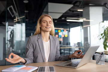 A businesswoman in a gray suit practicing mindfulness meditation at her office desk, promoting...