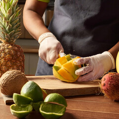 hands with gloves peels tropical fruit on kitchen background