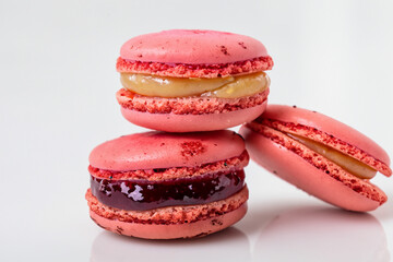 Three red macarons with jelly filling. Macaroons on a background. A macaroon with pink strawberry and white jam lying on a white background. Pink macaroons lying on a white background lifestyle with.
