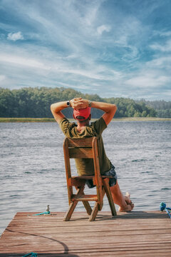 A man sits on a boat dock by the lake and enjoys the beautiful, idyllic nature in summer.