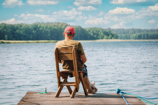 A man sits on a boat dock by the lake and enjoys the beautiful, idyllic nature in summer.