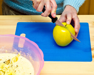 Making cookies. The cook has added walnut and starts to cut apple.
