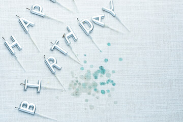 Silver letter candles spelling out Happy Birthday placed on a textured tablecloth with candle wax remnants. Celebrating a joyful birthday.