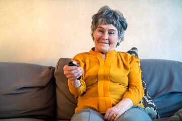 Old woman watches TV, holds a remote control.