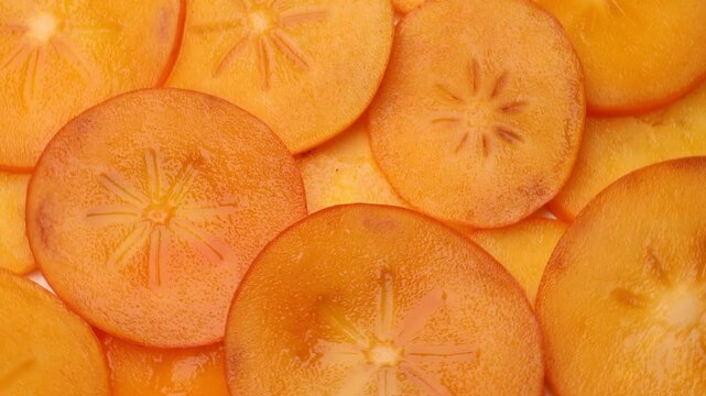 Slices of fresh persimmon rotating in a circle. Vibrant orange persimmon (kaki) slices turning, showcasing texture and color. 