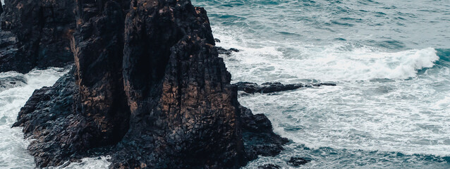 A dark rocks amist stromy wavy ocean in a cloudy weather.