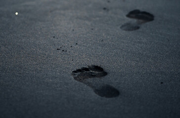 A black volcanic sand on a beach closeup with a person footprints.