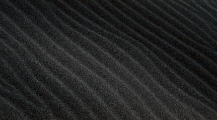 An abstract dark background with wavy black sand closeup.