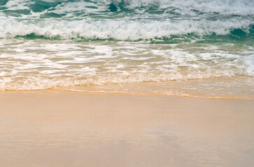A sandy beach on the coastline of the ocean with clear water with small waves.