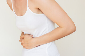 A young woman in white clothes holding her stomach with both hands, experiencing severe acute...