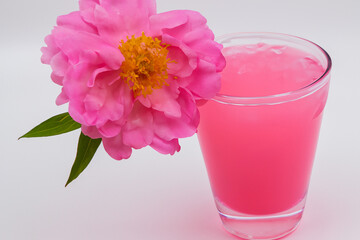 Pink drink with flowers in it. Woman is drinking pink drink on gray background. Woman is standing next to a flower and drinking ice. A pink flower with a gray background and a pink lifestyle ice.