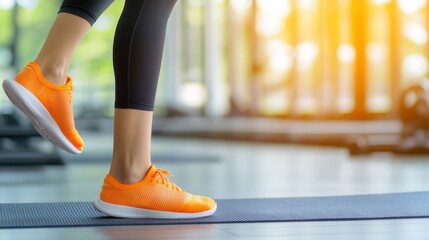Close-up of a woman wearing bright orange sneakers, exercising indoors on a mat with sunlight streaming into the gym.