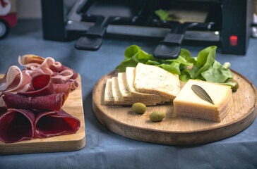 An inviting raclette spread featuring melted cheese, salami, ham, and vegetables. A perfect...