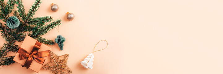 A flat lay composition of Christmas gift, fir branches, and decorative ornaments on a beige background. Top view, copy space