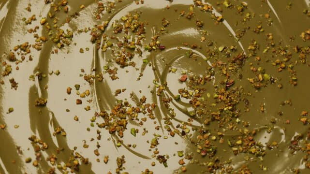 Rotating pistachio paste with crushed nuts in motion. Smooth, creamy pistachio spread garnished with crushed pistachios. texture, vibrant green color, and nutty details.  