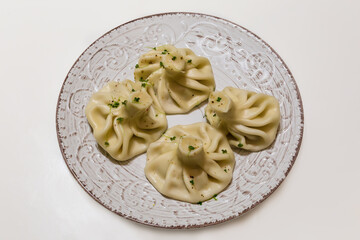 Boiled khinkali on gray-brown dish on white table