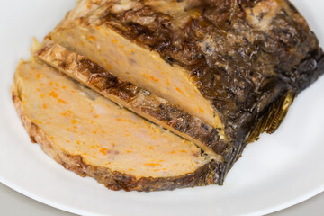 Partly sliced stuffed carp piece on dish, close-up