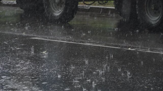 Large drops of rain water fall on asphalt road near parked truck. Heavy drops during rainstorm on road. Difficult weather conditions for driving, handheld shot.