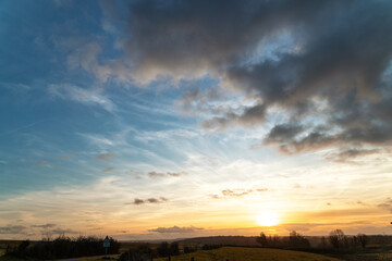 Sky and clouds for a background for a photo.A serene sunset scene with a dramatic sky. Dark clouds blend with warm orange and golden hues, casting a tranquil ambiance over distant treetops.