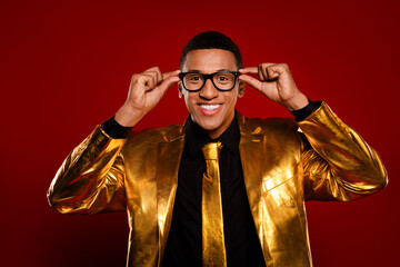 Charismatic young man in a striking golden suit smiling confidently against a bold red backdrop.