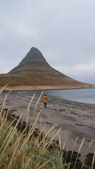 Dziewczyna w żółtej kurtce spacerująca po plaży z widokiem na skałę Kirkjufell. Zachodnia Islandia półwysep Snæfellsnes. 