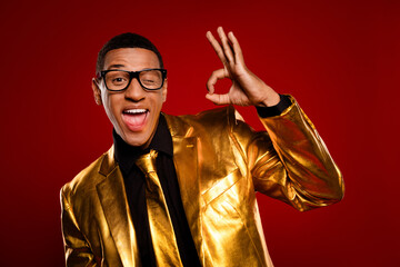 Charming young man in a stylish golden suit playfully winking with a vibrant red background