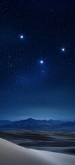 Four bright stars shining in a dark blue night sky over white sand dunes and dark mountains in the horizon, creating a beautiful and serene desert landscape