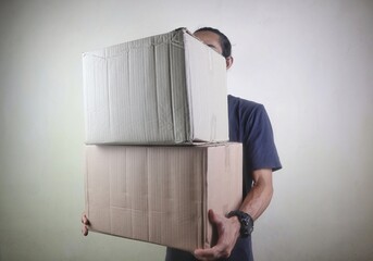 Asian young man is moving a pile of cardboard boxes inside the house against the wall background