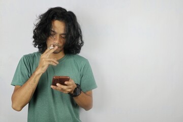young man with long hair is smoking while holding a smartphone