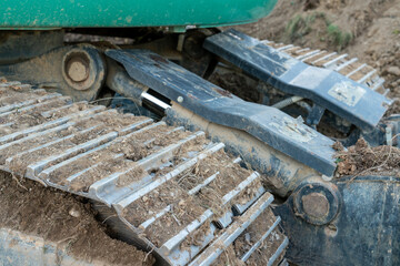 Closeup of excavator chain and gear from the side and front. Huge amount of ground already collected on the mechanical parts from working.