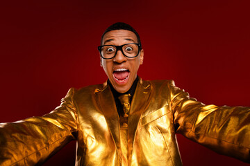 Energetic young man in a glossy gold suit with a vibrant red background, exuding charisma and joy, perfect for festive occasions