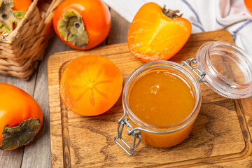 Persimmon jam with slices of ripe persimmon on wooden textured table. Delicious persimmon jam. Marmalade. Healthy sweets. Vegan. Close-up. Space for text. Copy space.