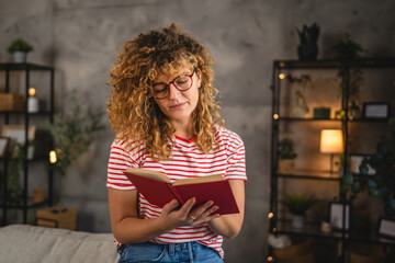 young adult woman with curly hair and eyeglasses read a book at home