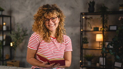 young adult woman with curly hair and eyeglasses read a book at home