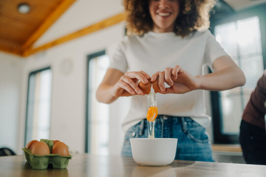 Woman cracking eggs into bowl in kitchen, preparing ingredients for baking