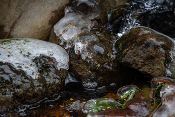 Close-up of rocks covered in ice and water, with visible moss and greenery, creating a textured and natural frozen scene.