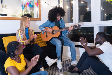 Friends clapping and having fun while man plays acoustic guitar at home