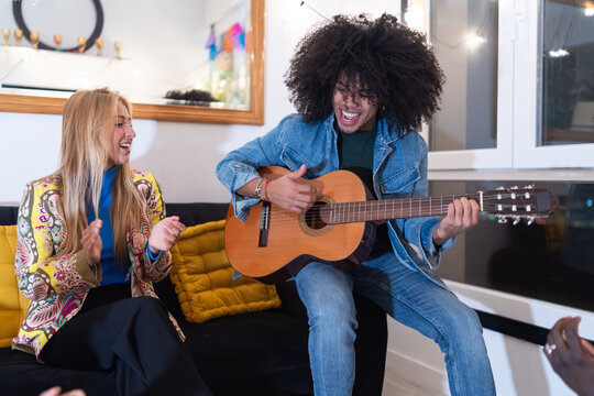 Friends playing acoustic guitar and clapping at home party
