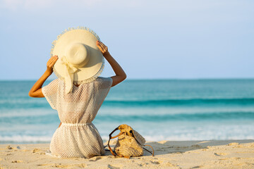 A female tourist sits on the white sand by the turquoise sea