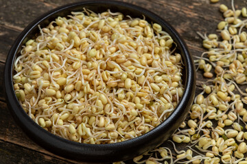 Home-sprouted mung beans with removed green skin in a bowl. Some sprouts lie on a rustic wooden table.