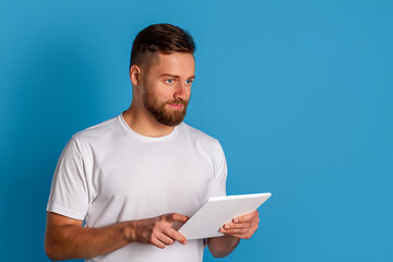Man holding tablet computer over blue background. Boy with tablet on blue background. Guy in blue technology with a white tablet. A young boy with a blue tablet and technology lifestyle on a white.