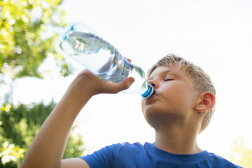 Little boy drinking water from bottle on a hot summer day, thirsty child drinks from water bottle...