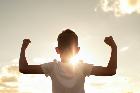 Silhouette of strong healthy active confident boy child flexing muscles feeling like a winner, child growth strength determination victory