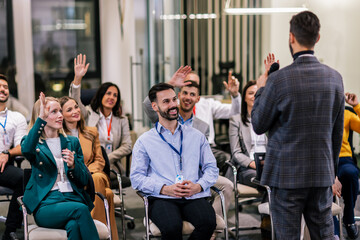 Young business man lecturing his multiethnic colleagues. Having a speech while holding a microphone. Everyone is listening and some are raising their hand.