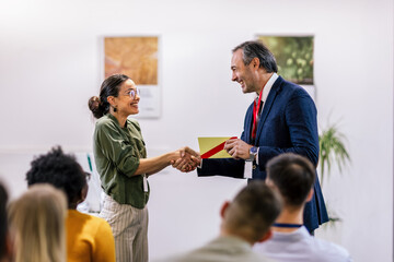 Front view of businesswoman receiving award from businessman in front of business professionals...